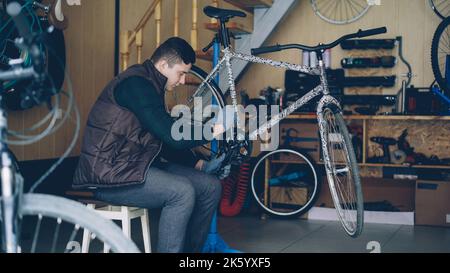 Ein erfahrener Meister repariert das Fahrradpedal mit einem Schlüsselschlüssel für Spezialwerkzeuge, während er in der Werkstatt mit zahlreichen Ersatzteilen und Geräten arbeitet. Menschen- und Wartungskonzept. Stockfoto