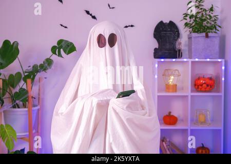 Der Halloween-Geist verwendet ein Mobiltelefon, um im Internet zu surfen, Online-Shops und Märkte zu durchsuchen. Der Geist macht an Halloween eine Bestellung von einem Smartphone. Neonlicht. Stockfoto