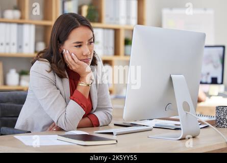 Gelangweilte junge Geschäftsfrau, die an ihrem Schreibtisch vor ihrem Computer sitzt und gelangweilt aussieht. Geschäftsleute, die an der Rezeption sitzen und sich aufregen, deprimiert aussitzen Stockfoto