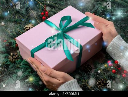 Frau Hände halten weihnachtsgeschenk oder Geschenkbox dekoriert Tannenbaum. Draufsicht auf die Hände einer jungen Frau, die ein Weihnachtsgeschenk in pi verpackt hält Stockfoto