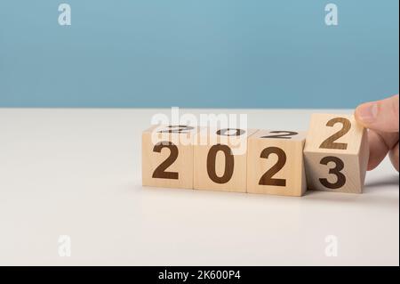 Mann Hand Flipping Würfel mit Jahr 2022 bis 2023. Neujahr Konzept. Hand hält Holzwürfel mit Klappblock 2022 bis 2023 Wort auf grauem Hintergrund Stockfoto