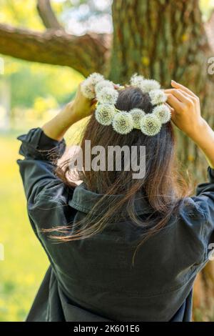 Glückliches Mädchen mit Kranz aus weißem Elendelion auf grünem Rasen am sonnigen Sommertag. Hochwertige Fotos Stockfoto