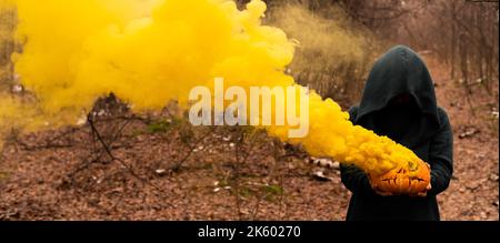 Eine gruselige Hexe hält einen dampfenden Kürbis in einen tiefen Wald. Jack o Laterne strahlt für halloween gelben Rauch aus Stockfoto