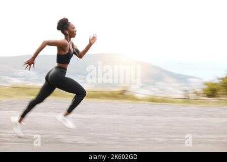 Eine afroamerikanische Athletin, die beim Laufen konzentriert auf ihre Ausdauer und Ausdauer schaut. Eine junge schwarze Frau, die draußen zu läuft Stockfoto