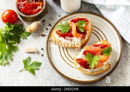 Offene Sandwiches oder Bruschetta mit gesalzenem Lachs, Käse und sonnengetrockneten Tomaten auf einem Steintisch. Gesundes Essen, Meeresfrüchte. Stockfoto