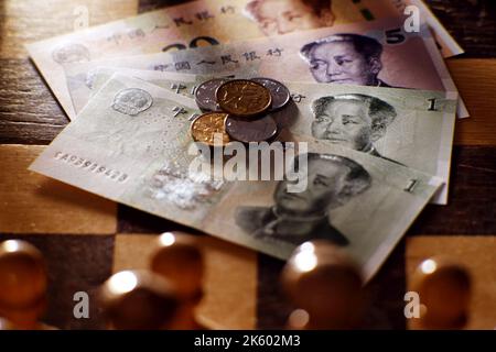 Chinesisches Yuan-Geld auf dem Hintergrund eines Schachbretts. Banknoten und Münzen von Yuan aus China auf dem Schachbrett Stockfoto
