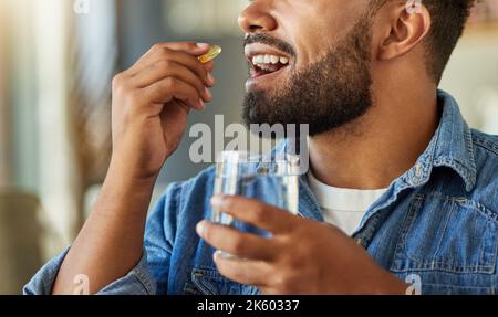 Bachelor Medikamente mit einem Glas Wasser trinken. Hispanischer Mann trinkt in seiner Wohnung eine Supplement-Kapsel. Mann mit einem Glas Wasser zu nehmen Stockfoto