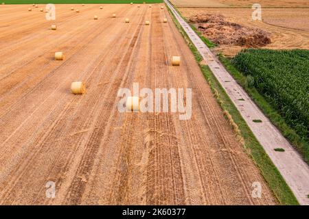 Ein Feld mit Heuballen sowie eine Schotterstraße, die von oben zum Horizont reicht, Deutschland Stockfoto
