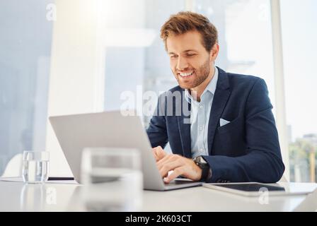 Ein glücklicher junger kaukasischer Geschäftsmann, der in einem Büro an einem Laptop arbeitet. Selbstbewusster männlicher Unternehmer plant beim Surfen im Internet und Senden Stockfoto