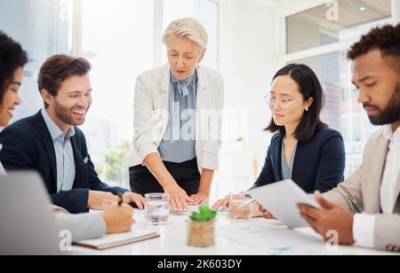 Eine reife kaukasische Geschäftsfrau, die während eines Meetings in einem Sitzungssaal eine Präsentation mit ihren verschiedenen Kollegen führt. Geschäftsleute gehen Stockfoto