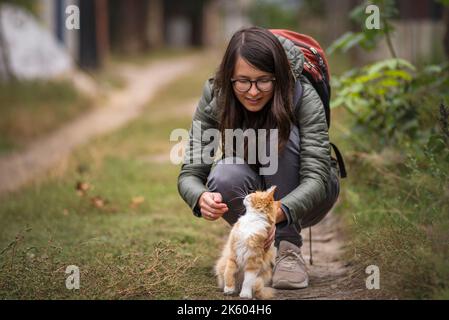 Porträt einer jungen Frau Brille mit niedlichen roten Katze mit grünen Augen. Weiblich umarmt ihre niedliche lange Haare Kitty. Hintergrund, Kopierraum, im Freien schöner Stockfoto