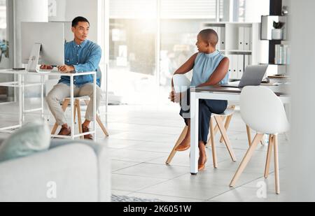 Zwei Geschäftsleute unterhalten sich, während sie in einem Büro zusammen arbeiten. Junger asiatischer Geschäftsmann im Gespräch mit einer afroamerikanischen Geschäftsfrau bei der Arbeit Stockfoto