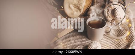 Gemütliche Winterkomposition mit einer Tasse Tee, Süßigkeiten und weihnachtslichtern auf Strickdecke. Banner mit Kopierfläche Stockfoto