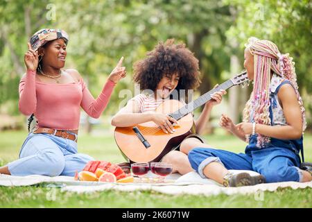 Schwarze Frauen, Freunde und Picknick im Park mit Gitarre, die Musik spielt, singt und Zeit miteinander verbringt. Komische, lustige und fröhliche Damen mit Akustik Stockfoto