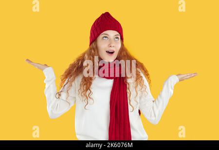 Mädchen trägt in rot gestrickten Schal und Hut zeigt mit fragen, welche Geste auf gelbem Hintergrund. Stockfoto
