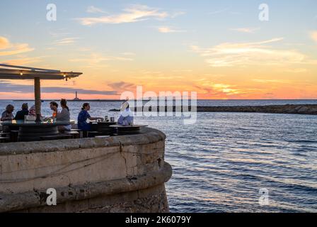 Menschen, die Speisen und Getränke im Freiluftrestaurant Buena Vista am mittelalterlichen Stadtwall am Meer in der Altstadt von Gallipoli, Apulien (Apulien), Italien, genießen. Stockfoto