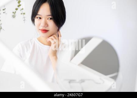 Gesichtspflege. Asiatische Frau. Anti-Aging-Verfahren. Hintergrund der Werbung. Ziemlich lächelnde Dame posiert mit Spiegel Licht Raum Innenraum Kopie Raum. Stockfoto