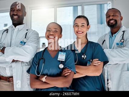 Eine Gruppe glücklicher Ärzte, die bei der Arbeit in einem Krankenhaus mit gekreuzten Armen stehen. Professionelle medizinische Fachkräfte, die lächeln und bei der Arbeit stehen Stockfoto