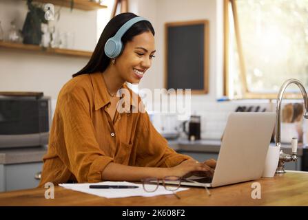 Junge, fröhliche Geschäftsfrau mit gemischter Rasse, die zu Hause an einem Laptop arbeitet und Papier und Rechnungen durchläuft. Eine glückliche hispanische Geschäftsfrau Stockfoto