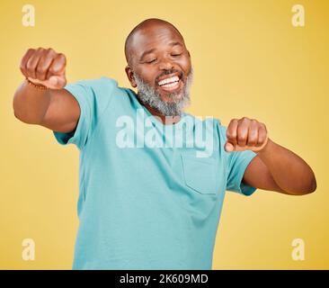 Ein reifer afrikanischer Mann, der ekstatisch aussieht, während er feiert und tanzt, indem er mit den Händen eine Faustpumpenbewegung macht und gegen ein Gelb singt Stockfoto