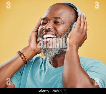 Ein reifer afroamerikanischer Mann, der mit kabellosen Kopfhörern Musik hört. Glücklicher Mann mit einem grauen Bart lächelt, während er Musik genießt. Augen geschlossen Stockfoto