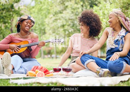 Freundinnen, Musik und Gitarre beim Picknick mit Obst, Getränken und glückliches Lachen in der Natur. Freundschaft, Gesang und Party auf Gras, Gruppe von schwarzen Frauen Stockfoto