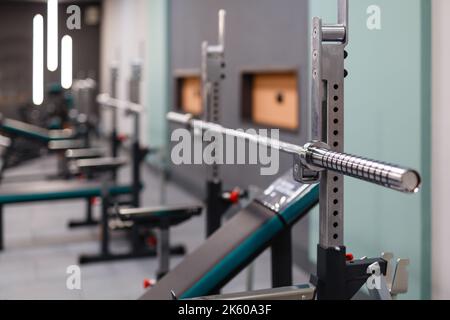 Vertikale Geräte für das Heben von Gewichts. Nahaufnahme einer leeren Langhantelbar ohne Teller auf dem Regal im Fitnessclub. Hochwertige Geräte und Wartung des Fitnessstudios. Auswahl Stockfoto