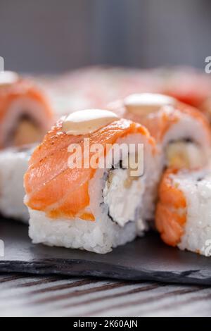Beliebtes Essen. Set von Philadelphia Sushi auf schwarzem Betonplatte auf dem Tisch. Nahaufnahme von Sushi-Brötchen mit Lachs und Käse und Aal Stockfoto