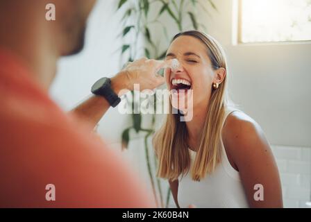 Nahaufnahme eines glücklichen jungen kaukasischen Paares, das sich im Badezimmer amüsieren kann. Fröhliche Frau lacht, als ihr Freund während des Spiels Schaumstoff auf die Nase schmiert Stockfoto