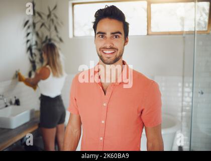 Porträt eines jungen kaukasischen Paares, das sich ein Badezimmer teilt, mit Fokus auf glücklichen jungen Mann, der lächelt und perfekte Zähne zeigt, während er die Kamera im anschaut Stockfoto