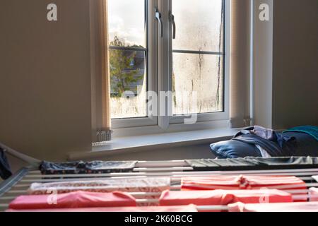 Kleidung, die auf einem Trockengestell in einer britischen Wohnung trocknet, wodurch im Herbst Kondenswasser auf der Innenseite der Fenster entsteht. Konzept: Feucht in Wohnungen, Mietprobleme Stockfoto