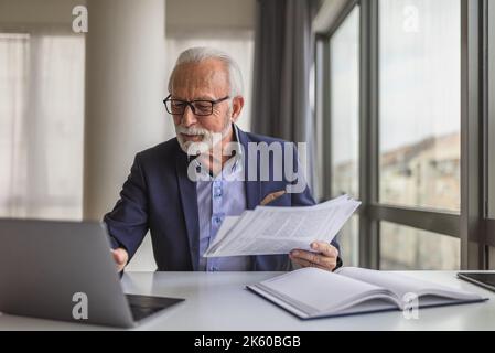 Bärtiger Senior Entrepreneur mit Brille, der seinen Arbeitskalender auf seinem Laptop im Sitzungssaal überprüft. Stockfoto