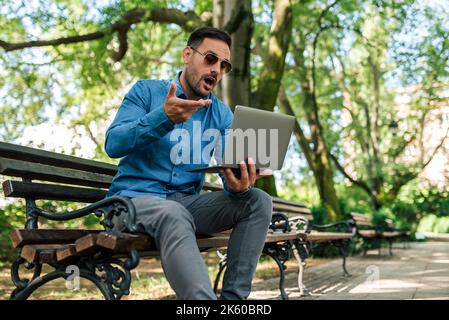 Bärtiger junger erwachsener Mann, der mit den Händen gestikulierte und seinen Kollegen im Park online etwas erklärte. Stockfoto