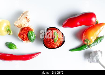 Ajvar-Sauce aus geröstetem rotem Pfeffer auf weißem Hintergrund mit Zutaten isolieren. Draufsicht Stockfoto