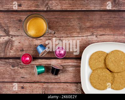 Kaffeekapseln, neben einer Tasse Kaffee und einem Teller mit Keksen Stockfoto