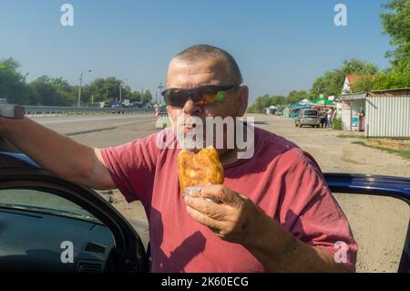 Porträt eines hungrigen ukrainischen Senior-Fahrers, der in der Nähe seines Autos Patty nahm, während er in der Nähe von Vasyliwka, Gebiet Saporischschja, Ukraine, stand Stockfoto