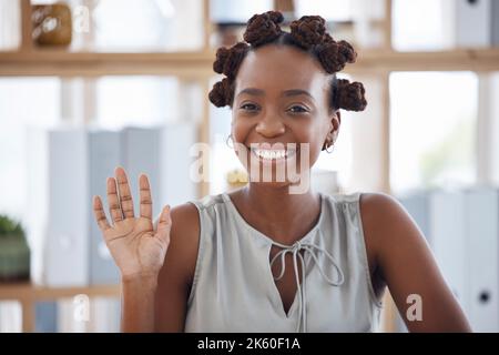 Eine junge, fröhliche afroamerikanische Geschäftsfrau winkt mit der Hand, während sie an einem Tisch in einem Büro sitzt. Fröhliche schwarze weibliche Geschäftsfrau macht eine Hand Stockfoto
