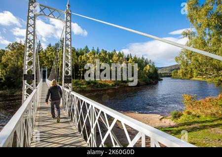 Ein Spaziergänger geht über die Hängebrücke Cambus O' May über den Fluss Dee in der Nähe von ballater in Royal Deeside, Aberdeenshire, Schottland Stockfoto