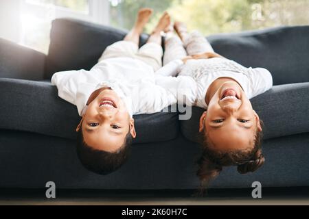 Portrait von zwei kleinen Geschwistern gemischter Rassen, die zu Hause auf dem Kopf liegend Zeit miteinander verbringen. Nette hispanische Mädchen und Junge spielen auf der Couch in der Stockfoto