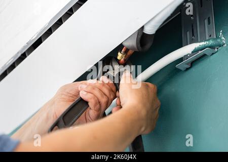 Mechaniker und Mechaniker. Professioneller männlicher Techniker arbeitet an der Installation von Klimaanlagen. Nahaufnahme der Hände eines männlichen Arbeiters, der Metall fixiert verwendet Stockfoto