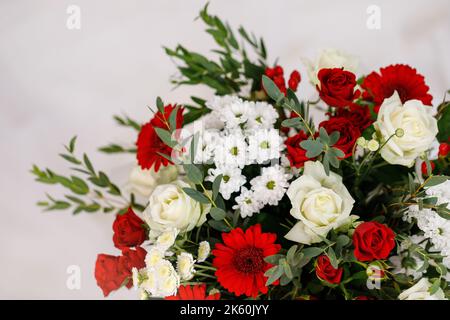 Blumenlieferung für jeden Urlaub. Großes Bouquet aus roten und weißen Blüten mit grünen Zweigen in weißem Geschenkpapier. Nahaufnahme von Rosen, Chrysanthemen, d Stockfoto