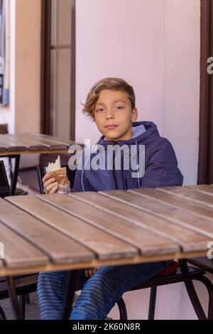 Niedlicher trendiger Teenager, der im Straßencafe Kebab isst. Street Food Konzept, gesunde Kindheit. Stockfoto