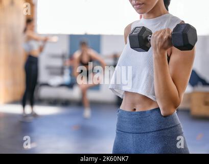 Nahaufnahme einer käukasischen Frau, die während des Trainings in einem Fitnessstudio mit einer Hantel Bizeps-Locken-Übungen macht. Weibliche Athletin fordert sich selbst durch Heben heraus Stockfoto