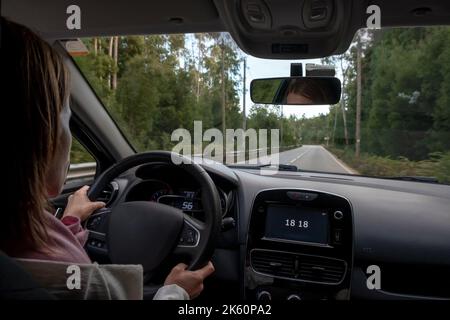 Fahrende Frau, Blick vom Rücksitz aus in einem niedrigen Winkel zum Armaturenbrett des Fahrzeugs. Aus dem POV des hinteren Beifahrersitzes. Stockfoto
