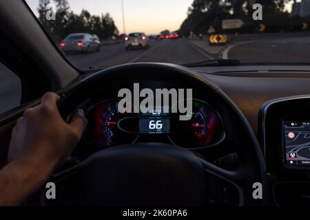 Fahreransicht auf dem Tachometer bei 66 km/h oder 66 mph auf einer stark befahrenen Straße, Nachtsicht im Herbst von einem Auto aus aus der Sicht des Fahrers auf die Straßenlandschaft. Stockfoto