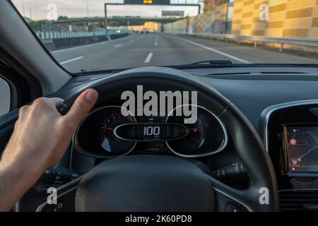 Fahreransicht auf den Tachometer bei 100 km/h oder 100 mph und unscharfe Fahrbahn, Sicht vom Fahrzeuginnenraum aus auf den Fahrer-POV der Straßenlandschaft. Stockfoto