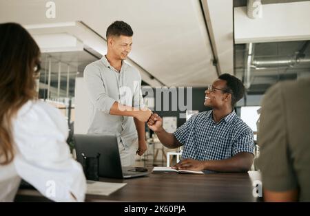 Zwei Geschäftsleute, die sich an einem Schreibtisch eine Faust bumsen. Mentor gratuliert dem Kollegen zu seiner guten Arbeit und seiner schnellen Lernrolle im modernen Büro Stockfoto