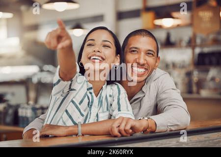Glückliches liebend gemischtes Rennpaar sitzt zusammen im Café. Aufgeregte junge Frau, die auf die Speisekarte zeigt und Getränke auswählt, während sie mit im Café sitzt Stockfoto