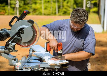 Der Zimmermann bohrt Holzbretter mit einem Schraubendreher ein, um sie zu verbinden Stockfoto