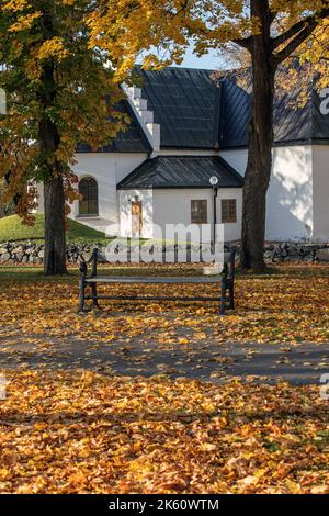 Holzbank mit herbstlichen Herbstblättern bedeckt. Bank vor der Kirche Stockfoto